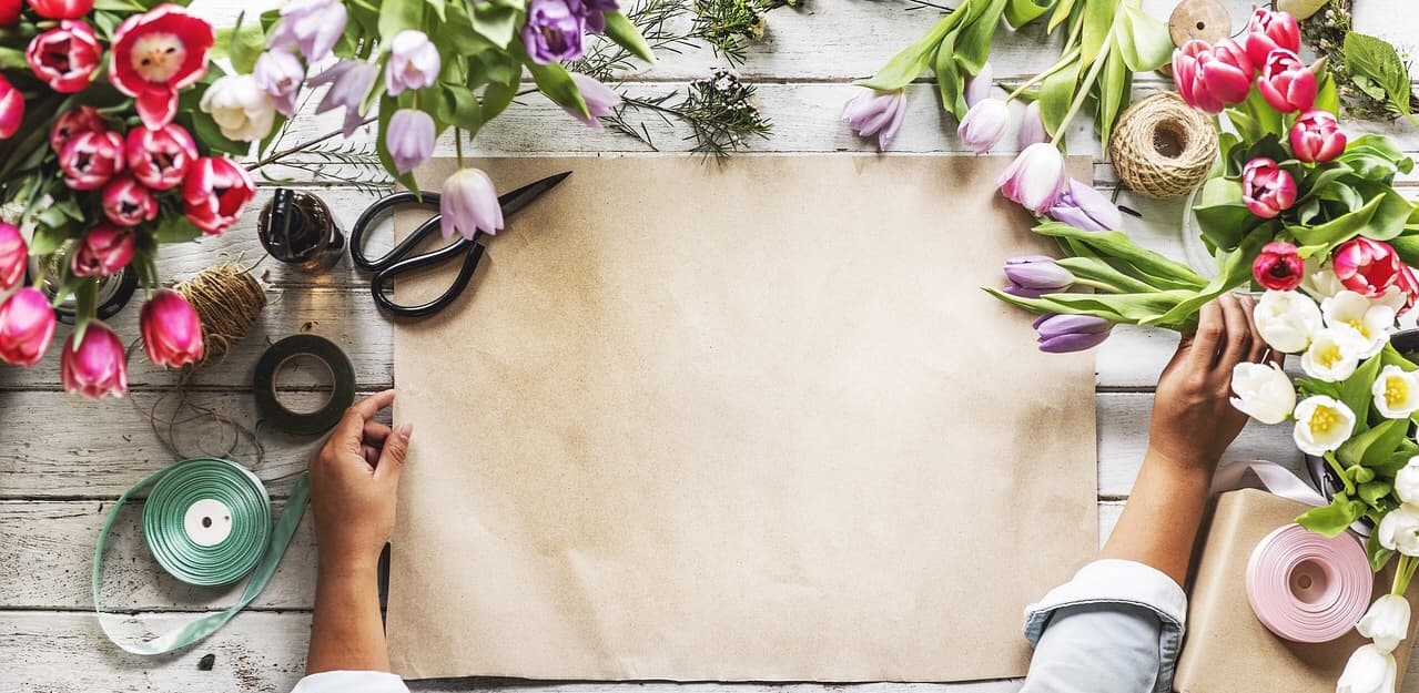 Arbeitstisch mit Packpapier, Schere, Bändern und Tulpen in Rosa, Lila und Weiß